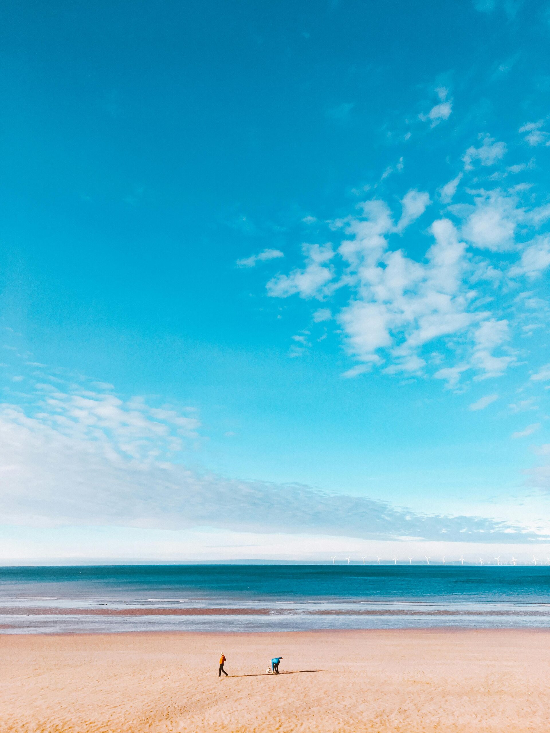 Tranquil scene of a lone walker on Colwyn Bay beach under a vast blue sky.